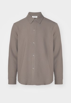 Camisa de manga larga con cuello en un material marrón suave, que presenta un cierre de botones en el frente, un dobladillo redondeado y una textura suave con un diseño minimalista.