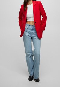 Rød skræddersyet blazer, hvid cropped top, lyseblå wide-leg jeans, sorte spidse sko. Glat stof, struktureret design, høj talje, let frynset kant.