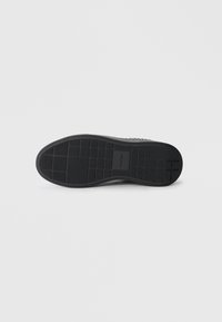 Black rubber shoe sole featuring a textured pattern with rectangular grips. Label embossed near the heel. Smooth finish overall.