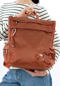 Orange tekstureret rygsæk med lynlåslukning øverst, forlommer og sølvfarvede hardware-detaljer. Har robuste håndtag og sidelommer.