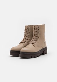 Stivali in pelle beige con punta rotonda, lacci frontali e una spessa suola in gomma marrone caratterizzata da un motivo di battistrada robusto.