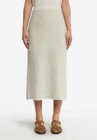 Stickad midiklänning i ljusbeige med ett strukturerat mönster, med en figursydd midja och en rak silhuett, i kombination med bruna sandaler.