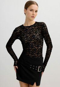 Bodysuit de encaje negro de manga larga con estampado floral, combinado con una falda negra de cintura alta que presenta un cinturón y acentos metálicos.