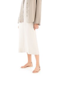 Beżowe skórzane sandały z szerokimi paskami i zestawieniem klamry. Biała podeszwa z lekko podwyższoną platformą. Noszone z lekką lnianą spódnicą i oversize'ową koszulą.