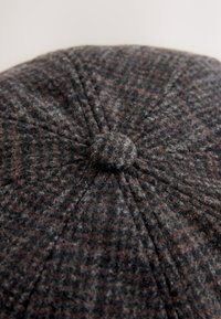 Vunena kapa u tamno sivoj i smeđoj uzorku psa zubića. Ima zaobljeni oblik, gornji gumb i finu teksturu s vidljivim vlaknima.