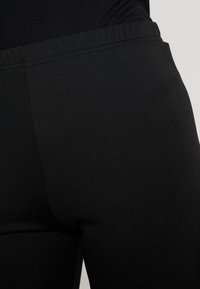 Czarne legginsy wykonane z elastycznego, gładkiego materiału o dopasowanym kroju. Posiadają elastyczny pasek w talii i brak widocznych szwów.