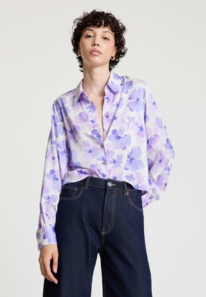 Chemise à fleurs violettes à boutons, coupe décontractée, avec manches longues et col classique. Associée à un pantalon taille haute en denim foncé.