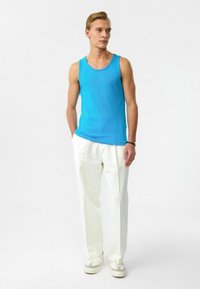 Blauwe katoenen tanktop met een ronde halslijn, gecombineerd met witte broek. Model draagt lichte sneakers. Minimalistisch ontwerp.