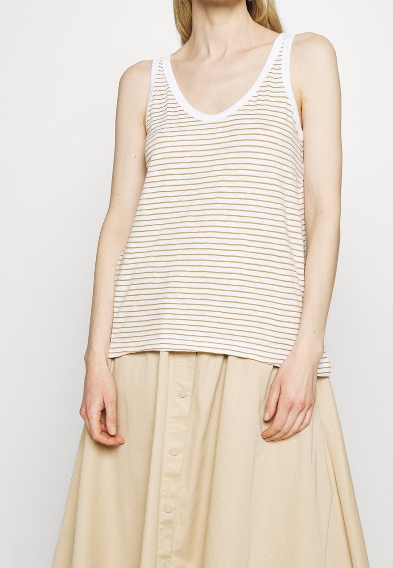 Femme portant un haut blanc sans manches avec de fines rayures beiges et une jupe beige boutonnée, vue des épaules jusqu’au milieu des cuisses.