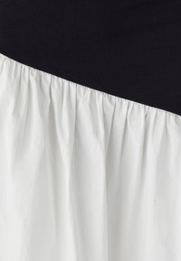 Melna un balta kleita ar melnu augšējo daļu un balto, sagurušo apakšdaļu. Mīksta tekstūra, gluda auduma virsma un asimetriska dizaina risinājums.