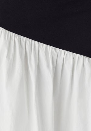 Černobílé šaty s černou horní částí a bílou, nabíranou dolní částí. Jemná textura, hladká tkanina a asymetrický design.