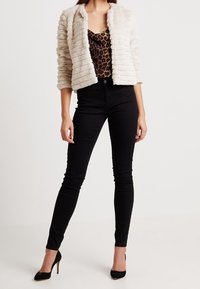 Krämfärgad fuskpälsjacka med texturerade ränder, kombinerad med en leopardmönstrad topp och svarta skinny jeans. Slim fit-design och högklackade skor.