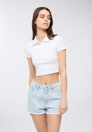 Polo shirt bianco corto con maniche corte e pattina con bottoni, abbinato a pantaloni corti in denim azzurro chiaro caratterizzati da orlo sfrangiato e dettagli strappati.