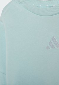 Light blue cotton sweatshirt featuring ribbed neckline and buttons on one shoulder; silver logo accents on the chest.