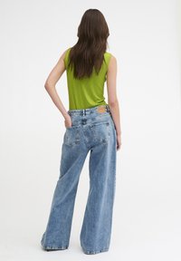 Zielona, prążkowana, bezrękawnik i szerokie, jasnoniebieskie dżinsy z tylnymi kieszeniami oraz skórzaną metką na pasku.