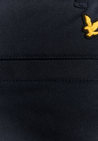 Mornarsko plava tkanina s teksturiranom površinom, koja ima horizontalni šav i zlatni ptica emblem utisnut u gornjem lijevom kutu.