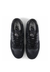 Ett par svarta New Balance 550 sneakers med snören, en blandning av mocka och läder, samt ett mönstrat hälkrage sett ovanifrån på vit bakgrund.