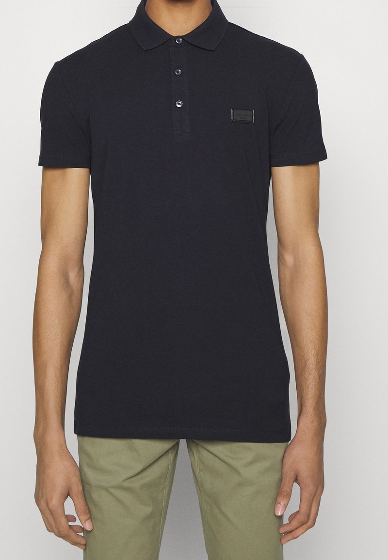 Polo en coton bleu marine avec un col, patte de boutonnage à trois boutons et un petit patch logo rectangulaire sur la poitrine.