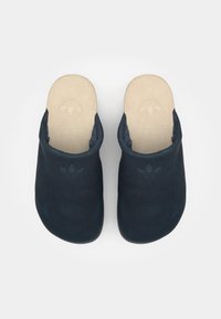 Námorné modré slip-on topánky s semišovým vrchom, zaoblenou špičkou a hnedou stielkou s embosovaným logom. Hladká textúra a minimalistický dizajn.