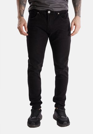 Jeans in denim nero con un design aderente, stile a cinque tasche, chiusura con bottone in metallo e dettagli di cucitura minimi, abbinati a sneaker nere.