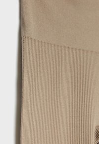 Leggings de color beige con textura acanalada, que presentan una sección superior lisa y una mitad inferior texturizada, destacando superficies contrastantes y detalles sutiles.