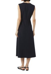 Robe sans manches bleu marine avec un buste ajusté, une silhouette en A, une longueur au genou et une fermeture éclair dans le dos. Portée avec des sandales plates noires.