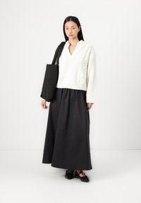 White knitted sweater with cable pattern, V-neck, paired with a black, floor-length skirt. Black tote bag and black shoes complete the look.