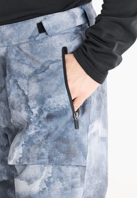 Grå och blå mönstrade byxor med en slät textur, som har en sidoficka med dragkedja och midjeband med kardborre.