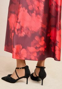 Voogav punase gradatsiooni seelik abstraktsete lillemustritega; kombineeritud musta seemisnahast pahkluu rihmadega kontsakingadega, millel on terav nina ja madal konts.