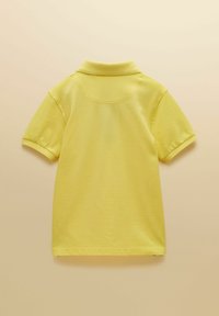 Żółta koszulka polo z krótkim rękawem i kołnierzykiem, widoczna z tyłu na jasnobeżowym tle.