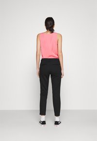 Svarta skräddarsydda byxor med slim fit, kombinerat med en ärmlös ljusrosa topp. Materialen verkar släta och lätta.