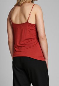 Top rosso senza maniche realizzato in un tessuto morbido con spalline regolabili, vestibilità leggermente ampia, orlo curvo, abbinato a pantaloni neri.