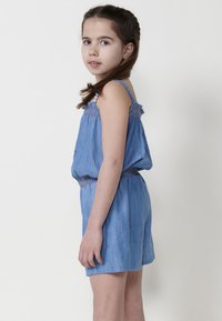 Džinsinis romperis su elastinga juostele, be rankovių dizainas ir spalvinga siuvinėjimo juosta viršuje. Šviesiai mėlynos spalvos, laisvo kirpimo.