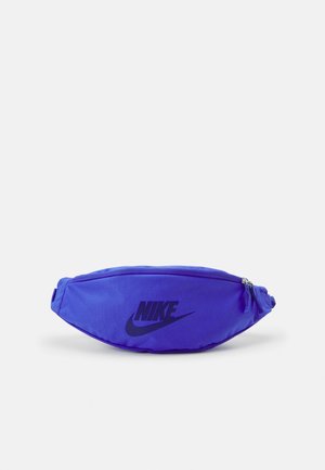 Sac banane Nike bleu avec logo noir, fermeture éclair et sangle ajustable, présenté sur un fond uni.