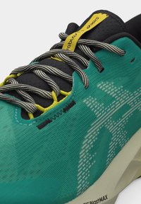 Τρέχον παπούτσι σε τιρκουάζ και μαύρο χρώμα με λευκό πουά σχέδιο, κορδόνια μαύρα και λευκά με ρίγες, κίτρινες θηλιές για τα κορδόνια και κίτρινη ετικέτα στη γλώσσα.