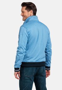 Lichtblauwe zip-up jacket met een hoge kraag, ribbelmanchetten en een marineblauwe tailleband. Bevat een gemêleerde stof en accentstiksels.