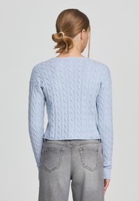 Maglione a coste color blu chiaro con maniche lunghe e scollatura rotonda, abbinato a jeans di denim grigi. Tessuto strutturato con polsini a coste.