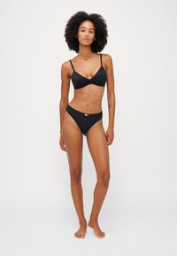 Čierny bikini set s trojuholníkovou podprsenkou s tenkými ramienkami a bikinami s nízkym pásom. Materiál je hladký s minimálnym hardvérom.