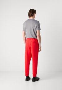 Grijze T-shirt met korte mouwen, gecombineerd met losse, rode joggingsbroeken met een elastische tailleband en ribgebreide manchetten. Zwarte sneakers maken de outfit compleet.