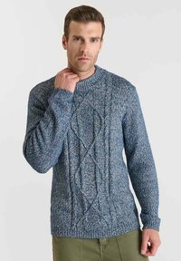 Blå stickad tröja med texturerade kabelmönster, rund halsringning och ribbade ärmslut och nederkant. Tyget har en blandning av ljusa och mörka trådar.