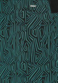 Tessuto nero con un motivo geometrico in teal, caratterizzato da angoli e linee nette. Include un piccolo etichetta in argento vicino alla parte superiore.