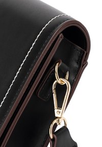 Schwarze Lederhandtasche mit glatter Textur, versehen mit weißen Nähten, braunen Akzenten und einem goldenen Metallverschluss zum Schließen.