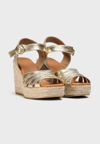 Sandales compensées métalliques dorées avec des brides entrecroisées, une sangle de cheville réglable et une semelle plateforme en jute texturé.