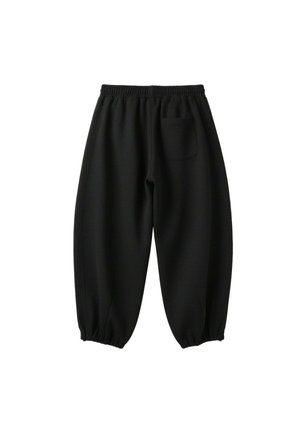 Femme portant une veste blanche zippée avec des rayures noires, un crop top noir et un pantalon noir ample sur un fond blanc uni.