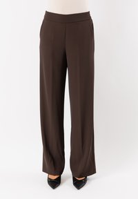 Pantaloni marroni a gamba larga realizzati in tessuto morbido, con vita piatta e tasche laterali, abbinati a scarpe nere con punta a teiera.