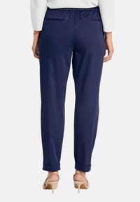 Marineblauwe broeken met een ontspannen pasvorm. Voorzien van een elastische tailleband, twee achterzakken en opgerolde mouwen. Glad stoftextuur.