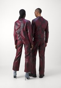 Burgundska kožna jakna i hlače s sjajnom završnom obradom, s prilagođenim krojem i krojenim šavovima, nosi ih dvije osobe s leđa.