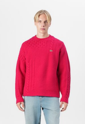 Chunky gebreide trui in felroze. Kenmerkt zich door textuurpatronen, een ronde halslijn en ribgebreide mouwen en zoom. Lacoste-logo op de borst.