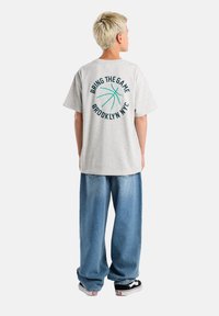 Light gray cotton t-shirt with short sleeves, featuring a green basketball graphic and text on the back, paired with loose blue denim pants.
