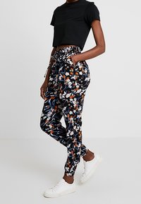 T-shirt cropped nera abbinata a pantaloni neri con un motivo floreale in arancione, bianco e blu, vita arricciata e polsini alla caviglia.